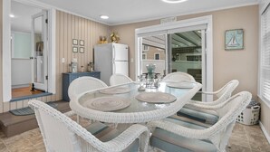 A dining area with a round glass table surrounded by white wicker chairs, a white refrigerator, and a blue cabinet. - Perfect vacation home : Cape Cod Charm & Comfort. Walk to private beach (Bourne)