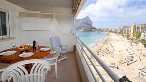 A balcony with a dining table, chairs, and a view of a beach with buildings and a mountain in the background. - Esmeralda by Interhome (Calpe/Calp)