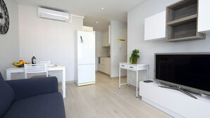 A modern, minimalist living space with a sofa, a dining table with fruit and a bottle, a white refrigerator, a TV, and a small plant on a white table. - Esmeralda by Interhome (Calpe/Calp)