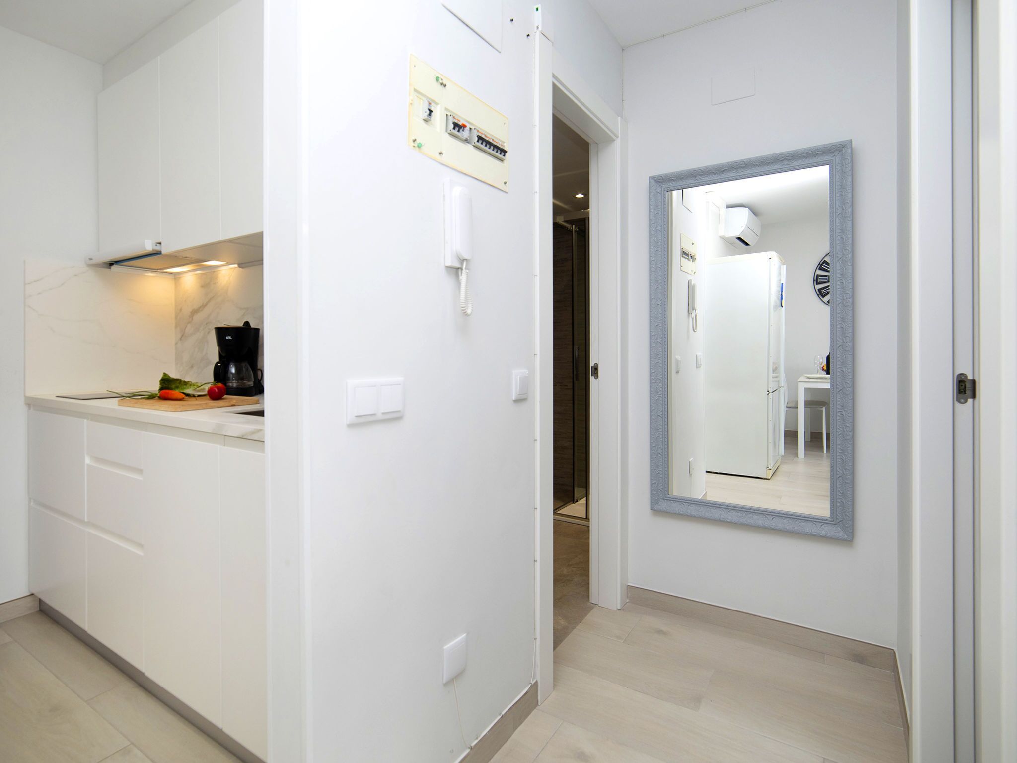 A modern kitchen with white cabinetry, a countertop with a coffee maker, and a small cutting board with vegetables.