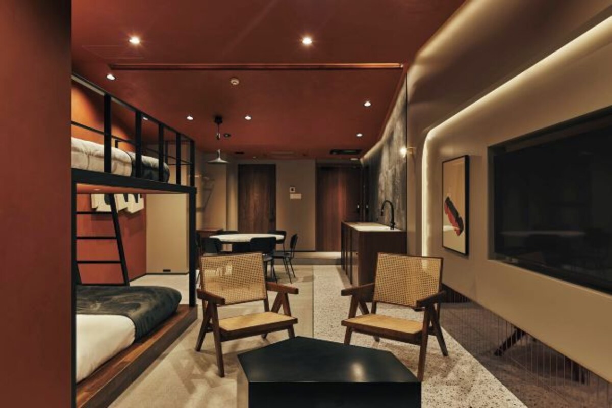 A modern hotel room with a bunk bed, a dining area, and a seating area with chairs and a table.