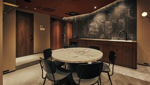 A modern kitchen with a round marble table and black chairs, a wooden door, and a textured wall. - illi Tria Shibuya (Tokyo)