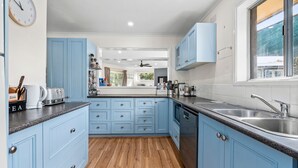 A modern kitchen with blue cabinets, a wooden floor, and a view of the backyard through the window. - The Abbey - Point Lonsdale (Point Lonsdale)
