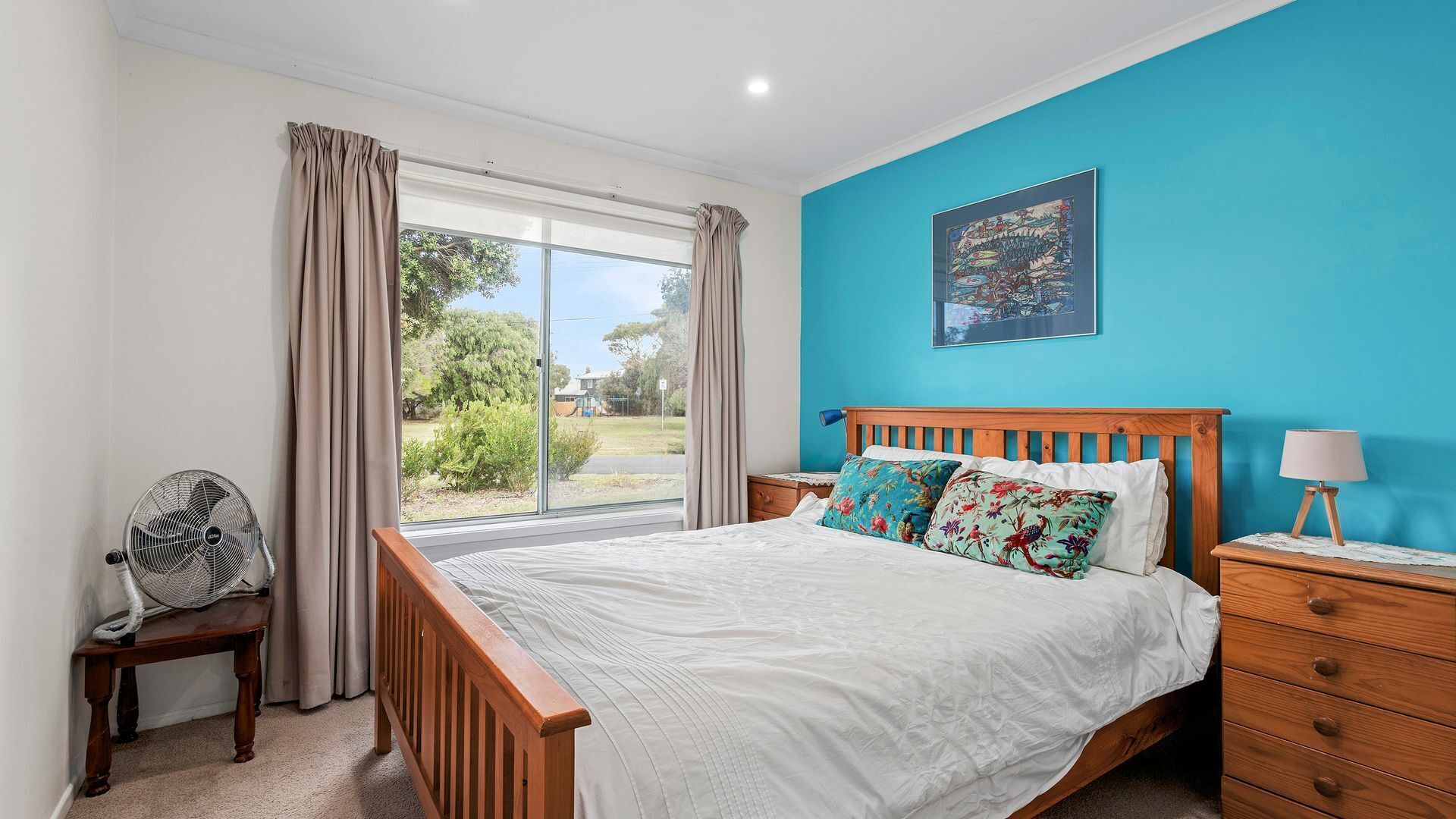 A bedroom with a bed, a nightstand, a chair, and a window with curtains.
