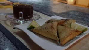 Ein Teller mit zwei Samosas und einem Teeglas auf einer Marmortafel.