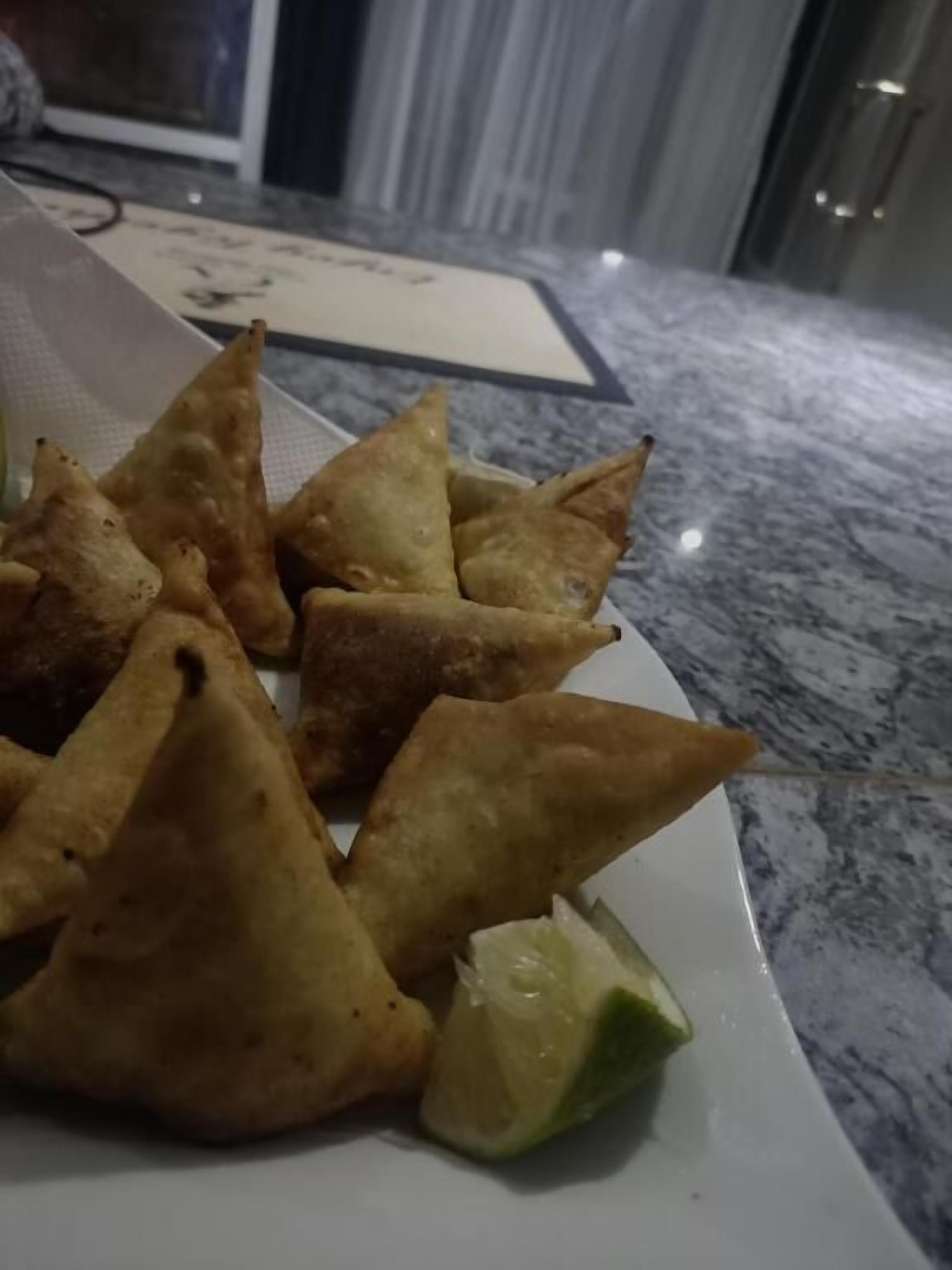 Ein Teller goldbraune Samosas auf einer Marmorplatte.