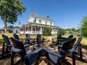 A white house with a green roof, a porch, and a fire pit with Adirondack chairs. - First Floor Suites at The Legacy Inn Harmony Floor (Luray)