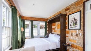 Une chambre à coucher avec un lit, des rideaux verts, une lampe, un tableau accroché au mur et un tableau d’affichage en liège avec des étiquettes.