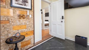 A hotel hallway with cork wall decor, a framed picture, a small table with a speaker, and a door leading to a bedroom. - The Legacy Suites Collection Full Property Rental (Luray)