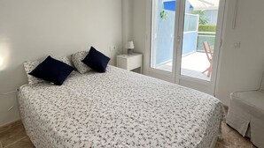 Een slaapkamer met een bed, twee kussens, een nachtkastje met een lamp en een raam met uitzicht.