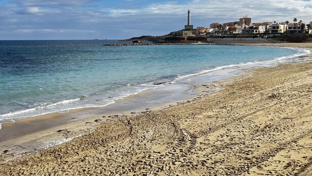 Une plage avec un ciel dégagé, un phare et des bâtiments en arrière-plan.