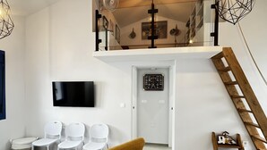 Un salon moderne avec un téléviseur, des chaises blanches, un fauteuil jaune et une échelle en bois.