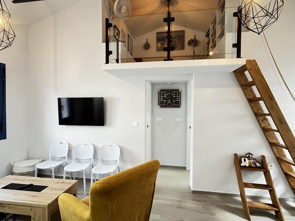 Una sala de estar moderna con televisor, sillas blancas, un sillón amarillo y una escalera de madera.