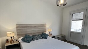 Ein ordentlich gemachtes Bett mit gemusterten Kissen, zwei Nachttische mit Lampen, ein Holz-Kopfteil und ein Fenster mit Jalousien.