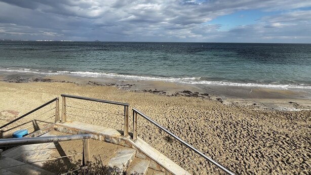 Ein Strand mit einer Treppe, die zum Ufer führt, einem Geländer und dem Meer im Hintergrund.