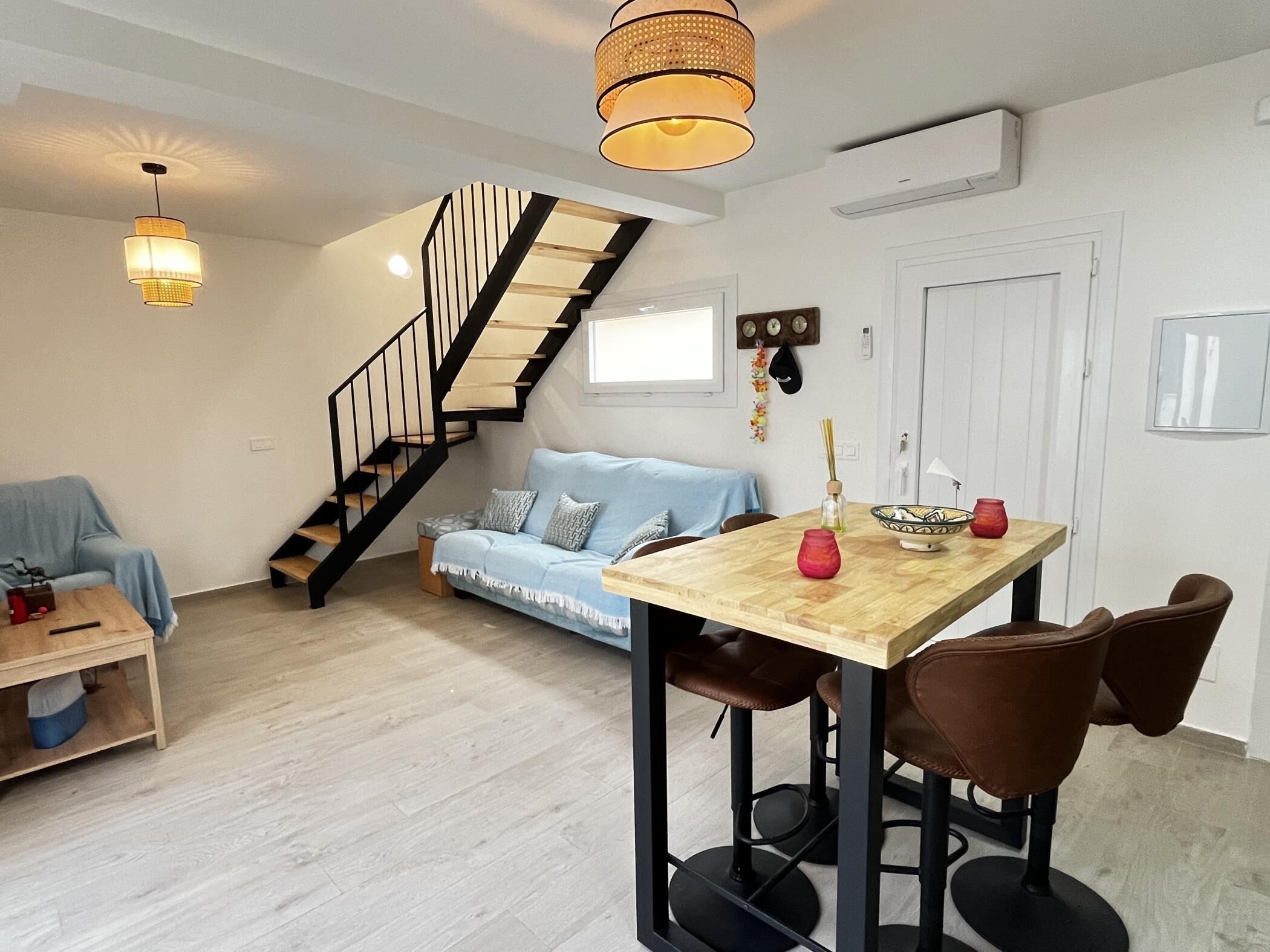 Una sala de estar moderna con una escalera, un comedor con una mesa y sillas de madera, y un sofá azul.