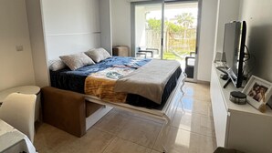 A bedroom with a bed, a TV, a desk, and a sliding door to a balcony. - Flat Aguamar, ground floor, 1 bedroom, garden and swimming pool. (Dénia)