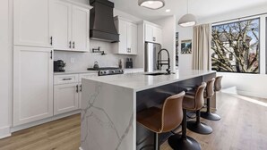 A modern kitchen with white cabinetry, a marble island, and bar stools. - Nashville 4-home retreat with rooftop hot tubs & game rooms, sleeps 48 (Nashville)