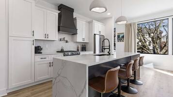 Una cocina moderna con armarios blancos, una isla de mármol y taburetes de bar.