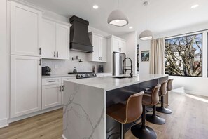 A modern kitchen with white cabinetry, a marble island, and bar stools.