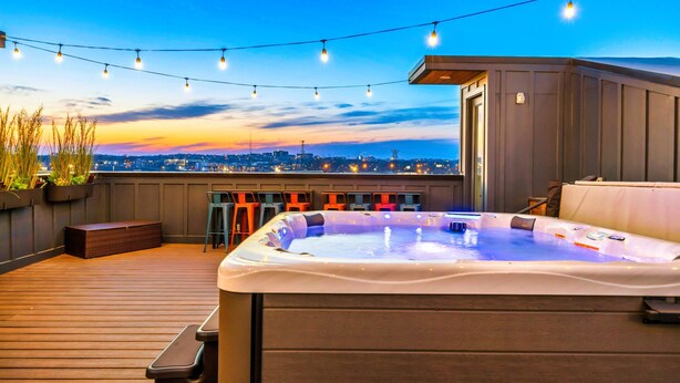 A rooftop deck with a hot tub, string lights, and a city view at dusk. - Nashville 4-home retreat with rooftop hot tubs & game rooms, sleeps 48 (Nashville)