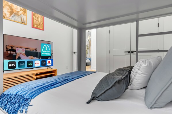 A modern hotel room with a large bed, a TV displaying streaming services, and a view of the outside.