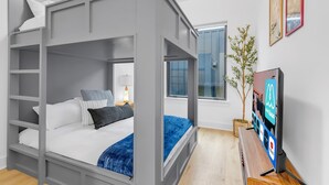 A modern bedroom with a bunk bed, a bedside table with a lamp, a TV, and a window with a view of the outside. - Nashville 4-home retreat with rooftop hot tubs & game rooms, sleeps 48 (Nashville)
