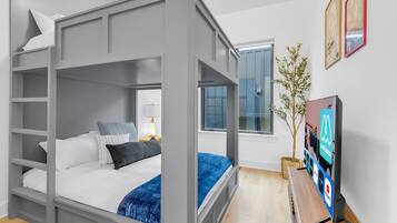 Un dormitorio moderno con una cama litera, una mesita de noche con lámpara, un televisor y una ventana con vistas al exterior.