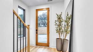 A modern hallway with a wooden staircase, a large wooden door, and two large potted plants. - Nashville 4-home retreat with rooftop hot tubs & game rooms, sleeps 48 (Nashville)