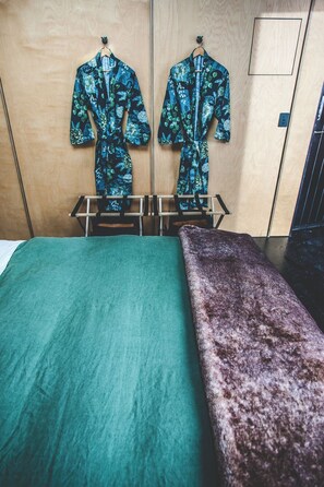 Un dormitorio con una cama, un banco y dos perchas con batas.