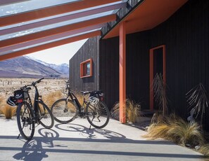 Een modern gebouw met een donkere gevel en oranje accenten, twee fietsen voor de deur, en een bergachtig landschap op de achtergrond.