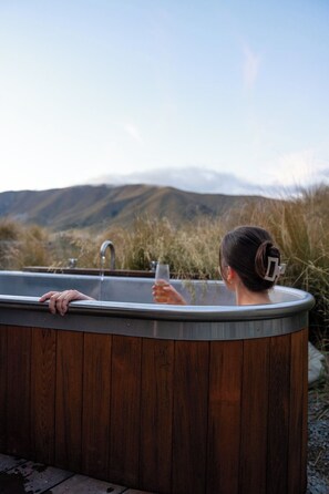 Un jacuzzi con revestimiento de madera, un grifo de metal y una persona sosteniendo un vaso.