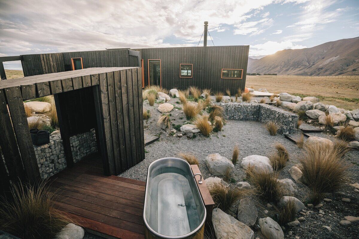 A rustic cabin with a wooden deck, a hot tub, and a stone wall.