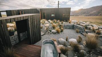 A rustic cabin with a wooden deck, a hot tub, and a stone wall.