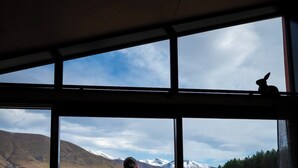 A couple standing on a wooden deck, looking out at a mountainous landscape through large windows. - Skylark Cabin – Private Luxury Escape with Hot Tub (Ben Ohau)