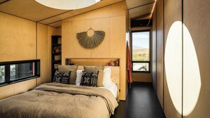 A modern bedroom with a large bed, a circular skylight, and a view of the outdoors. - Skylark Cabin – Private Luxury Escape with Hot Tub (Ben Ohau)