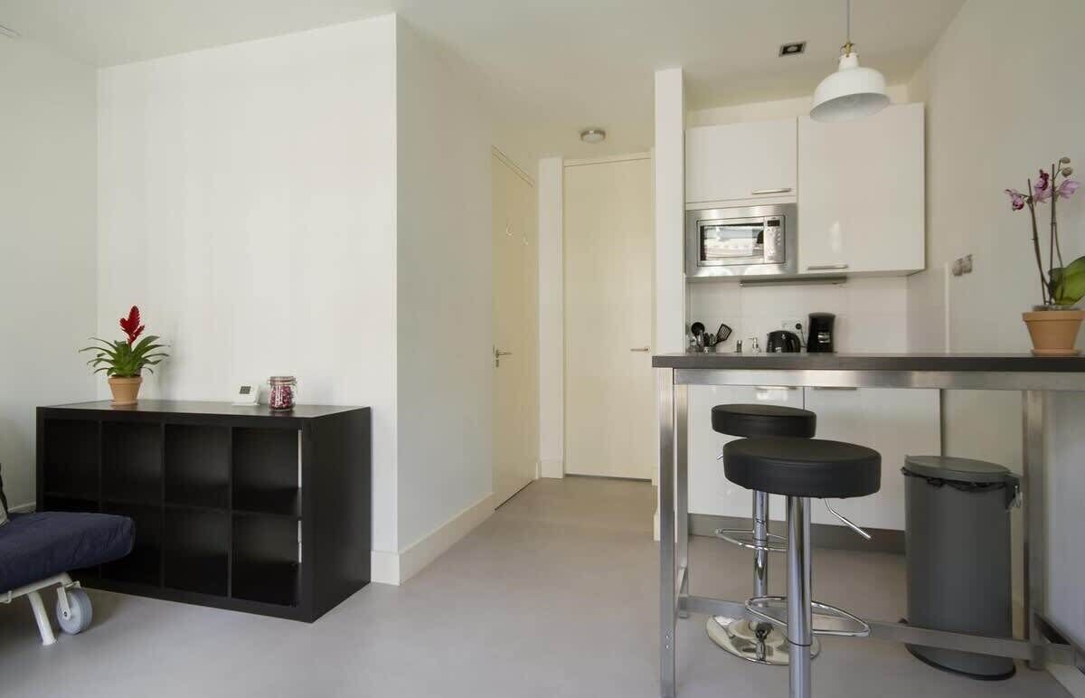 A modern kitchen with a microwave, coffee machine, and bar stools. There is a black console table with a potted plant and a small table lamp.
