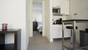 A compact kitchen with a microwave, coffee maker, and a small dining area with a bar stool.