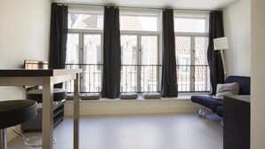 A modern living room with a sofa, a dining table, and a window with curtains.
