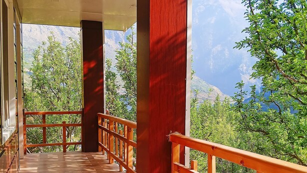 A wooden deck with a railing, leading to a covered area with a view of mountains and trees.