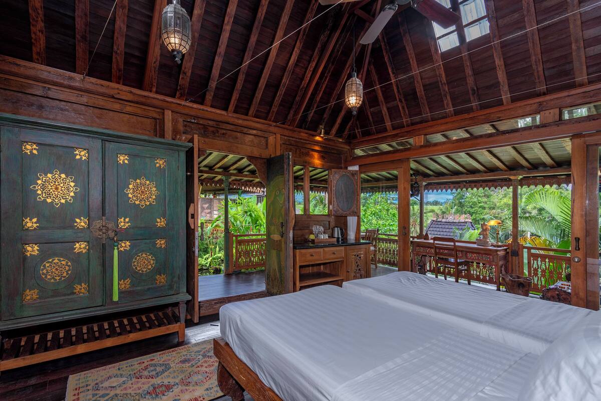 A spacious room with a large bed, wooden furniture, and a view of lush greenery.