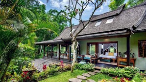 A traditional-style building with a covered porch, a bed with a canopy, and a garden with stone pathways. - Lumina Sanctuary (Ubud)