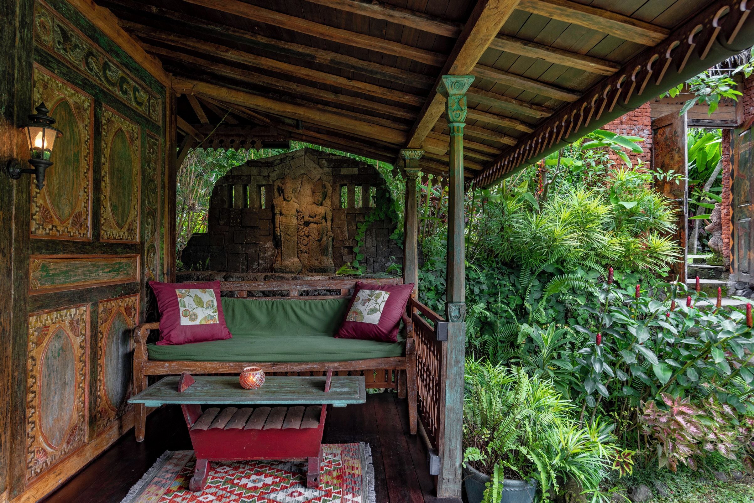 A wooden porch with a bench, a stone wall, and lush greenery.