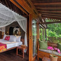 Una habitación con cama, un banco y vistas al exterior con vegetación.