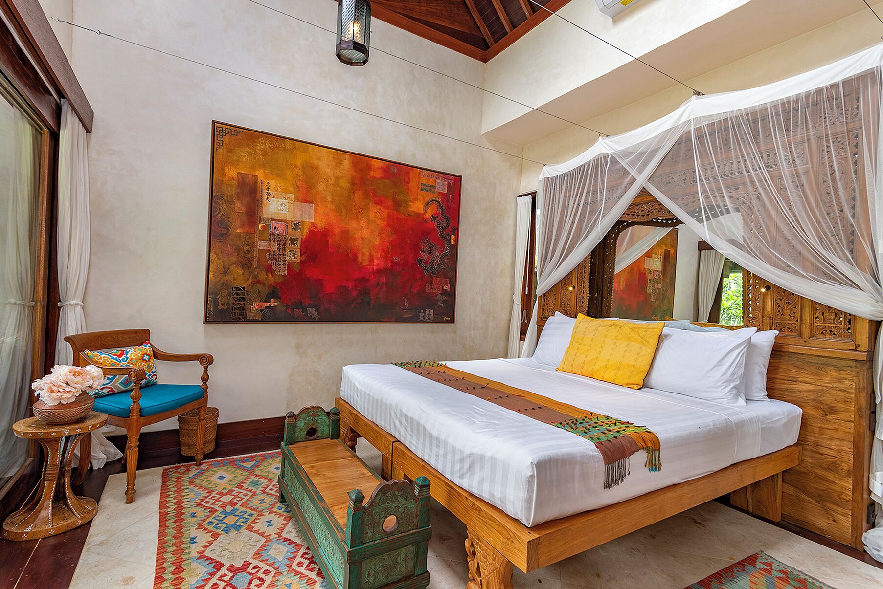 A room with a bed, a chair, a table, and a large painting on the wall.