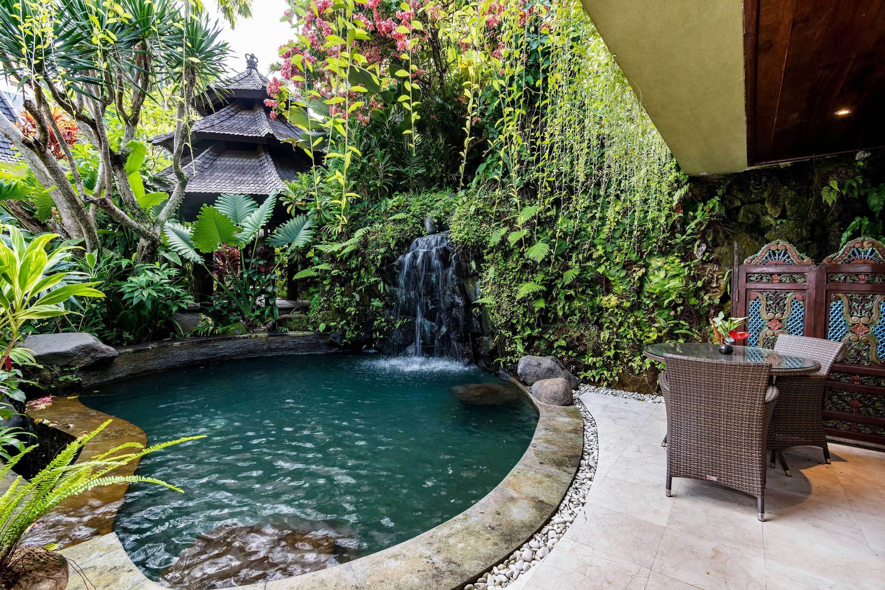 A tranquil indoor garden with a small waterfall, a traditional-style gazebo, and a wicker table.