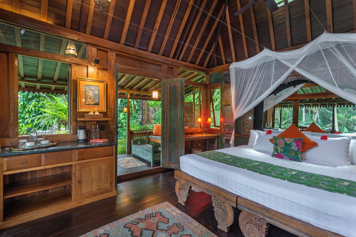 A wooden bedroom with a canopy bed, a wooden desk, and a view of lush greenery outside.