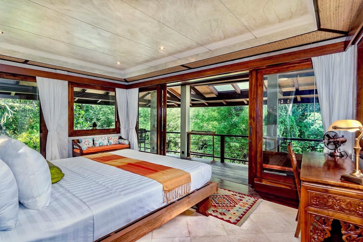 A bedroom with a bed, a desk, and a view of greenery.