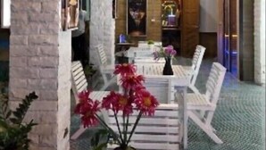 A restaurant with white chairs and tables, a chandelier, and a potted plant with pink flowers.