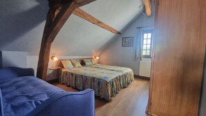 Een slaapkamer met schuine balken plafond, een bed met bloemenbeddengoed, bedlampen, een raam met gordijnen en een radiator.